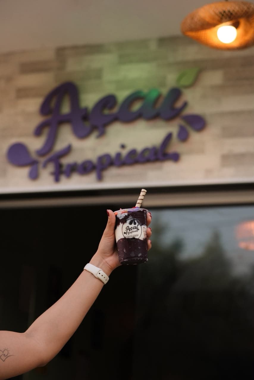 Fachada da Açaí Tropical com cliente erguendo um copo de açaí