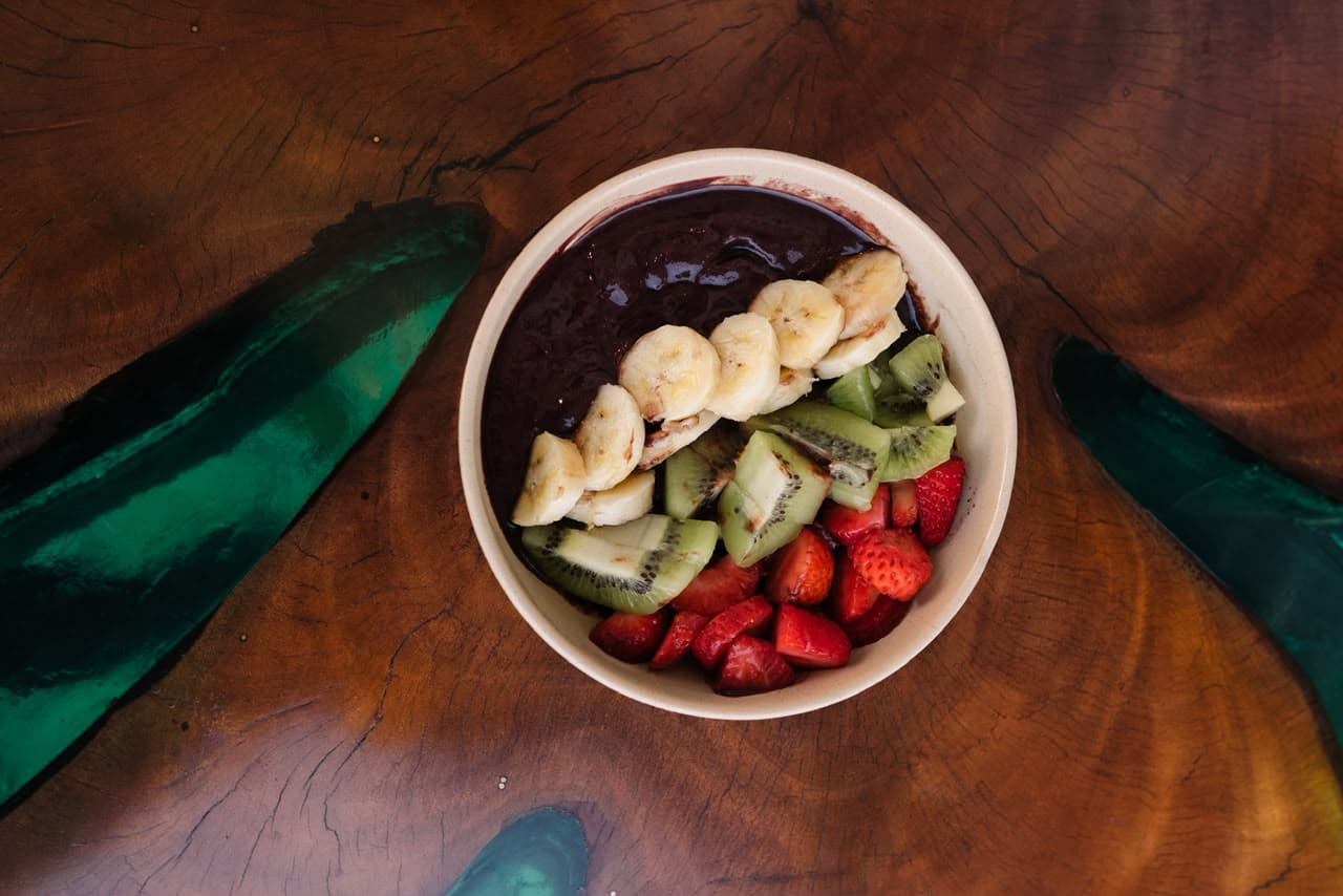 Tigela de açaí com banana, kiwi e morango sobre mesa de madeira